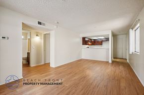 Santa Ana apartment for rent - A spacious room with wooden floors and white walls, with a logo for Beach Front Property Management in the bottom left corner.