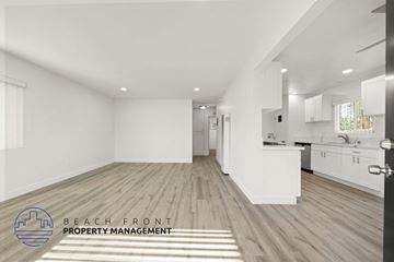 Tustin apartment for rent - A spacious, well-lit room with wooden flooring and white walls, featuring a kitchen area with white cabinets and appliances.