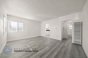 Monterey Park apartment for rent - A spacious room with wooden flooring and white walls, with a logo for Beach Front Property Management in the bottom left corner.