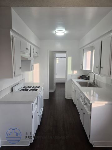 Norwalk apartment for rent - A clean, white kitchen with dark wood floors and a logo for Bel-Air Property Management in the bottom left corner.