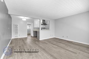 Long Beach apartment for rent - A spacious room with wooden flooring and a logo for Beach Front Property Management in the corner.