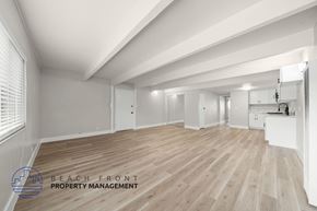 Anaheim apartment for rent - A spacious room with wooden flooring and white walls, with a logo for Beach Front Property Management in the bottom left corner.