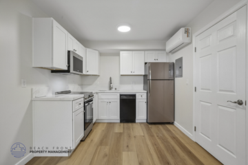 Long Beach apartment for rent - A kitchen with white cabinets and appliances, a wooden floor, and a door on the right.