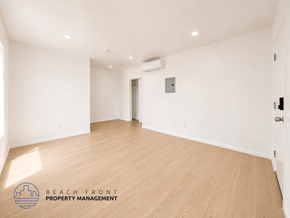 San Pedro apartment for rent - A spacious room with wooden flooring and white walls, with a logo for Beach Front Property Management in the bottom left corner.
