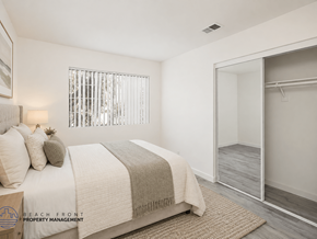 Orange apartment for rent - A bedroom with a bed, a window with blinds, a rug, and a mirror.