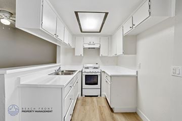 Los Angeles apartment for rent - A kitchen with white cabinets and appliances, with a logo for Beach Front Property Management in the bottom left corner.