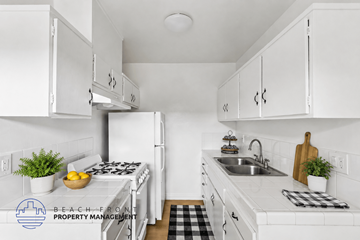 Hawthorne apartment for rent - A kitchen with white cabinets and appliances, a black and white checkered mat on the floor, and a logo for Beach Front Property Management in the corner.
