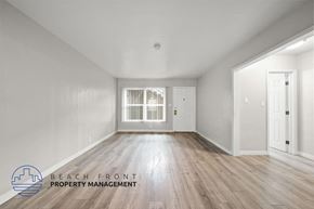 Long Beach apartment for rent - A spacious room with wooden flooring and white walls, with a logo for Beach Front Property Management in the bottom left corner.