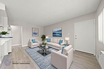 Downey apartment for rent - A living room with a white couch, a blue rug, and a painting on the wall.