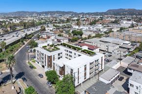 Los Angeles apartment for rent - A modern building with a green roof is surrounded by other buildings and a busy street.