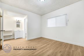 Huntington Park apartment for rent - A room with wooden floors and white walls, with a logo for Beach Front Property Management in the bottom left corner.