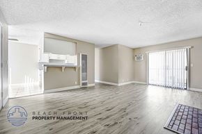 Hawthorne apartment for rent - A spacious room with wooden flooring and a logo for Beach Front Property Management in the corner.