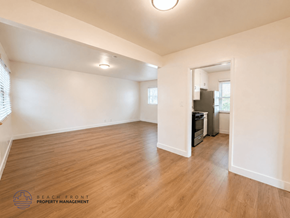 Redondo Beach apartment for rent - A spacious room with wooden flooring and white walls, with a logo for Beach Front Property Management in the bottom left corner.