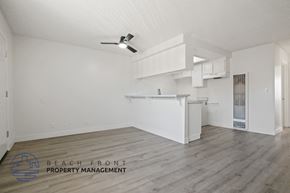 Torrance apartment for rent - A spacious, empty room with a ceiling fan and a logo for Beach Front Property Management.