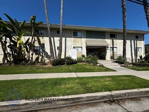 Torrance apartment for rent - A building with a white door and windows is surrounded by greenery.