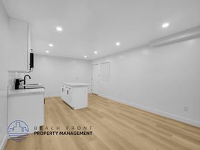 Long Beach apartment for rent - A spacious room with wooden flooring and white walls, featuring a kitchenette and a refrigerator.