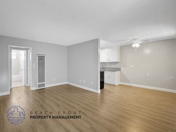 Long Beach apartment for rent - A spacious room with wooden flooring and a logo for Beach Front Property Management.