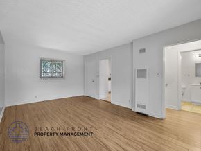 Los Angeles apartment for rent - A spacious room with wooden flooring and white walls, with a window and a door visible.