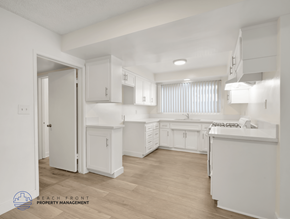 Inglewood apartment for rent - A white kitchen with wooden floors and a logo for Beach Front Property Management in the bottom left corner.