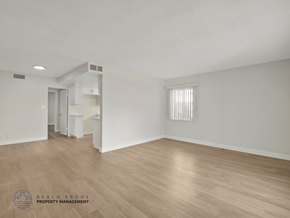 Inglewood apartment for rent - A sparsely furnished room with a logo for Beach Front Property Management in the bottom left corner.