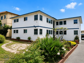 Redondo Beach apartment for rent - A white two-story building with a blue stripe on the roof and a garden in front.