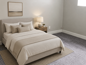 Downey apartment for rent - A bed with a white comforter and pillows is in a room with a lamp and a picture on the wall.