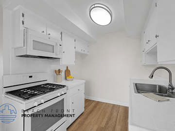 Downey apartment for rent - A kitchen with white cabinets and a black stove top oven.