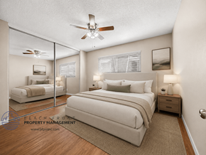 Downey apartment for rent - A bedroom with a large bed, a ceiling fan, and a mirrored wall.