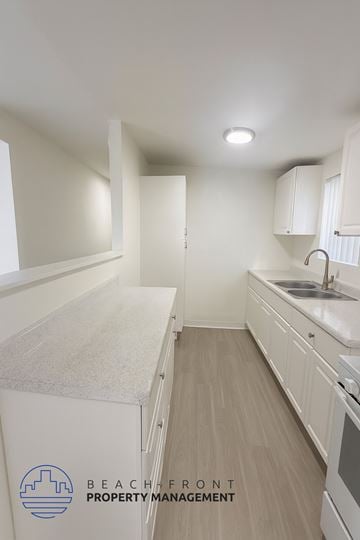 Anaheim apartment for rent - A kitchen with white cabinets and a logo for Beachfront Property Management.