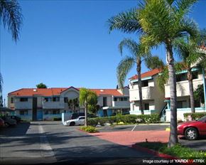 Paramount apartment for rent - A building with a red roof and a parking lot in front.