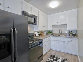 Bellflower apartment for rent - A black refrigerator is in a kitchen with white cabinets.