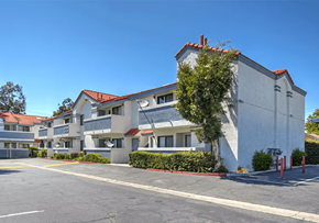 Paramount apartment for rent - A building with a red tile roof and white walls with a tree in front of it.