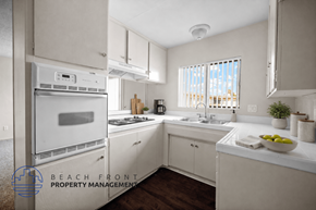 Inglewood apartment for rent - A kitchen with white cabinets and appliances, a window with blinds, and a bowl of fruit on the counter.
