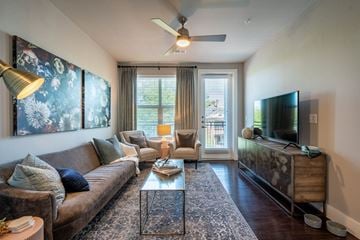 Dallas apartment for rent - A living room with a brown couch, a glass coffee table, and a television on a wooden cabinet.