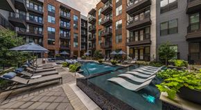 Richardson apartment for rent - A pool surrounded by lounge chairs and umbrellas in a courtyard.