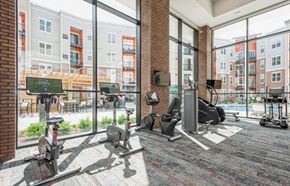 Warrenville apartment for rent - A gym with a brick wall and a view of apartment buildings outside the windows.