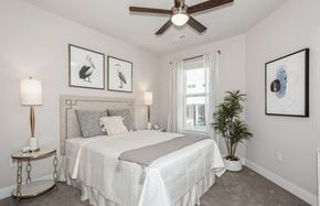 Warrenville apartment for rent - A bedroom with a bed, a ceiling fan, and a potted plant.