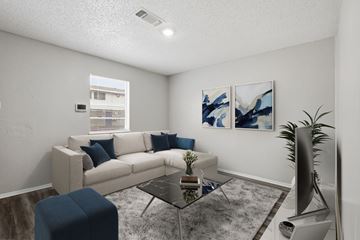Stephenville apartment for rent - A living room with a white couch, a blue ottoman, a glass coffee table, and two abstract paintings on the wall.