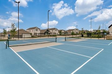 Fort Worth apartment for rent - A tennis court with a blue surface and white lines, surrounded by a fence and houses in the background.