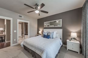 Katy apartment for rent - A bedroom with a large bed, a ceiling fan, and a mirror above the bed.