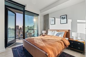 San Diego apartment for rent - A bedroom with a large bed and a view of the city through the window.