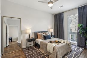 Nashville apartment for rent - A bedroom with a large bed, a ceiling fan, and a view of a building outside the window.