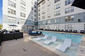 Dallas apartment for rent - A large swimming pool with lounge chairs and a bar area in front of a modern apartment building.
