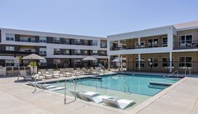 Omaha apartment for rent - A large swimming pool surrounded by lounge chairs in front of apartment buildings.