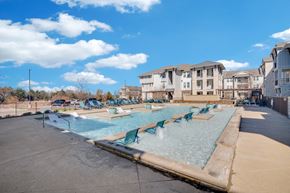Rockwall apartment for rent - A swimming pool with chairs around it and apartment buildings in the background.