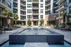 Dallas apartment for rent - A large pool in the middle of a courtyard surrounded by lounge chairs and palm trees.