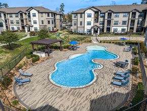 Conroe apartment for rent - A large swimming pool with a wooden deck and lounge chairs.