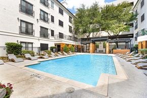 Dallas apartment for rent - an outdoor pool with lounge chairs and trees in front of an apartment building