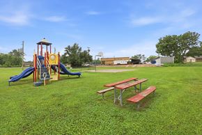 Stephenville apartment for rent - A playground with a yellow and blue slide, a red and white picnic table, and a green lawn.