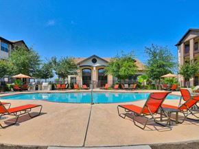 New Braunfels apartment for rent - A swimming pool surrounded by red chairs and umbrellas.